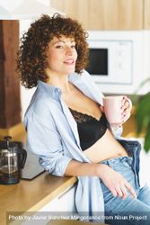 Woman relaxing in kitchen with hot drink while leaning on counter, vertical composition 5X9OG4