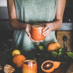 Woman holding glass of freshly squeezed blood orange juice, square crop