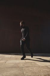 Stylish Black man walking on pavement in dark clothes