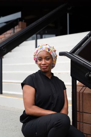 Portrait of confident Black nurse in head covering sitting on steps in front of medical building