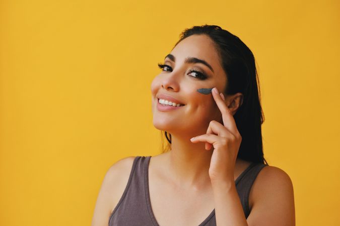 Smiling Latina woman applying clay mask with hand