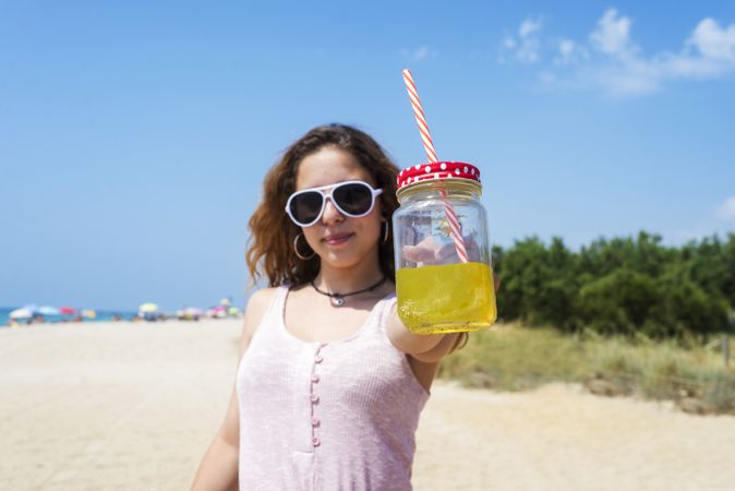 A young woman in dress and sunglasses, holding out a delicious juice drink in her hand