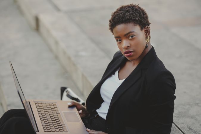 Stylish Black woman with laptop on steps near handbag