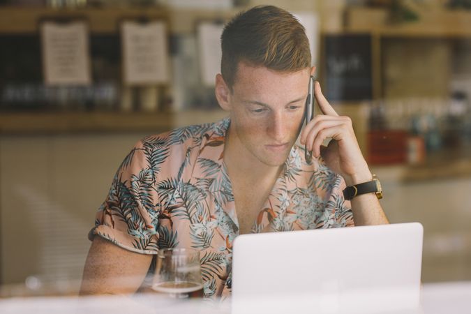 Man talking on smartphone while browsing laptop