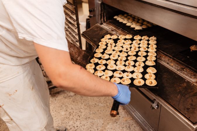 Bald baker checking pastry inside oven