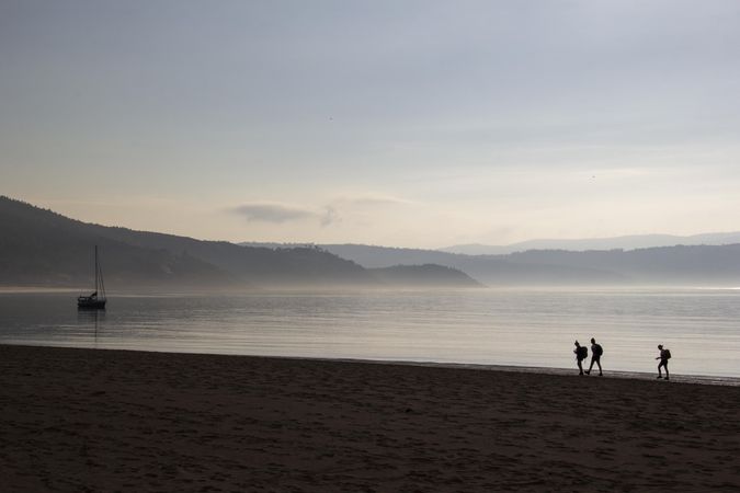 Silhouette of three people with backpacks walking on beach