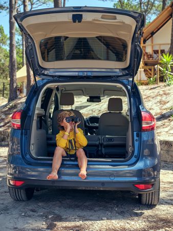 Boy sitting in car and looking through binoculars