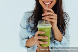 Close up of smiling woman drinking fresh juice with straw on light background 49BQ6b