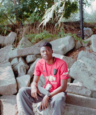 Young man in red shirt sitting on rocks beside tree