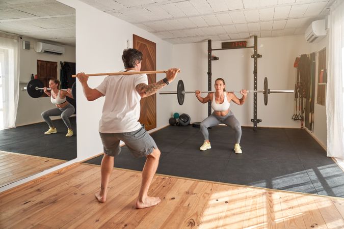 Trainer guiding athlete exercising with barbell in gym