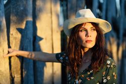 Female brunette leaning against wooden fence outside at dusk