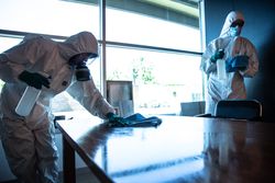 Two people in PPE sanitizing meeting room in an office during lockdown