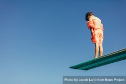 Boy standing on diving spring board against blue sky 0JVR80