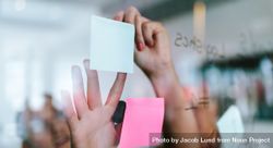 Hands of woman pasting sticky notes on glass wall in office 43A2g0