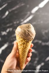 Hand holding chocolate ice cream cone on marble background 5Xzykb
