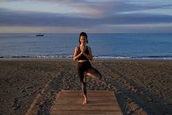 Content Hispanic woman practicing Vrikshasana posture near sea