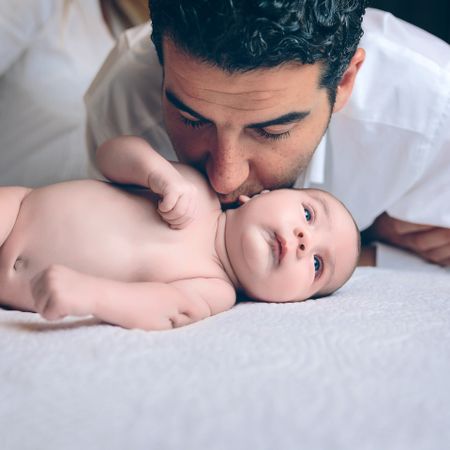 Man kissing to peaceful newborn lying over bed