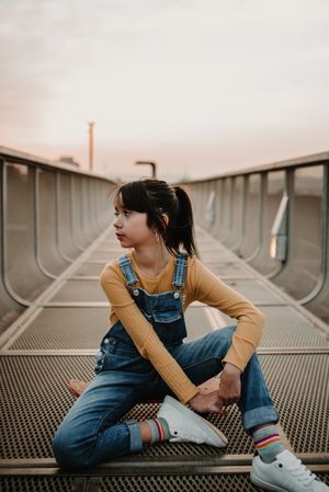 Girl sitting on skateboard on walkway