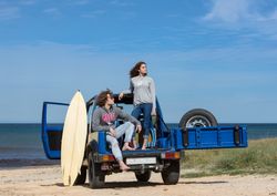 Guy with surfboard and woman on roof of car