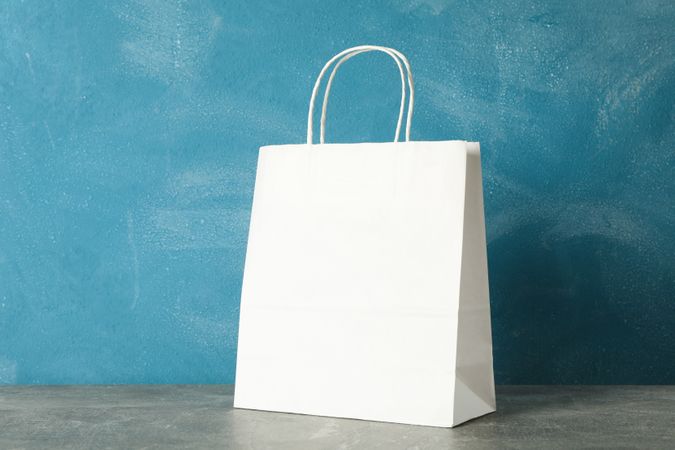 paper bag on grey table against blue background, copy space