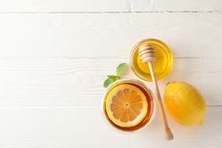 Glass of tea with lemon, mint, honey and dipper on wooden background, top view