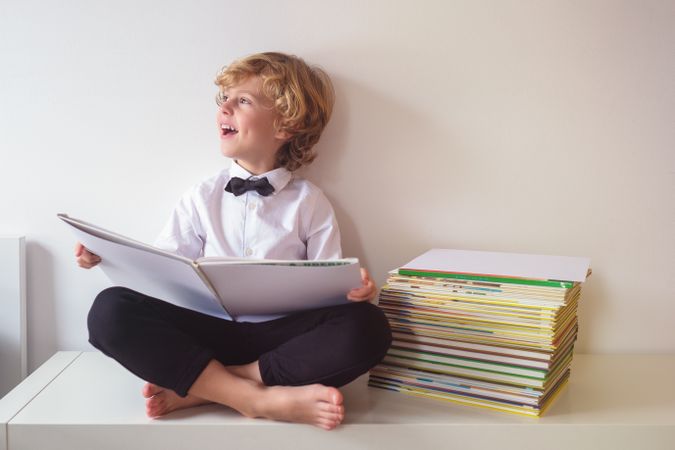 Happy schoolboy reading book in room