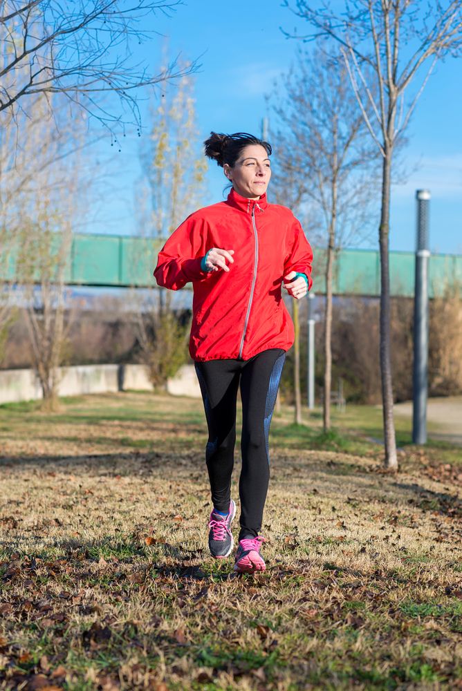 Fit woman in red running outdoors in the grass on sunny fall day