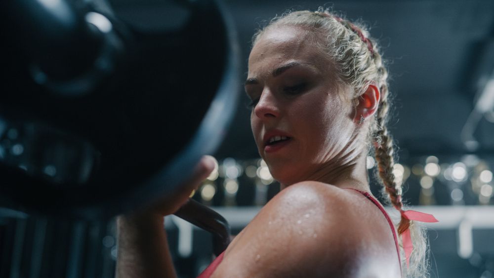 Professional Female Athlete Lifting Heavy Barbell and Training in a Dark Gym.