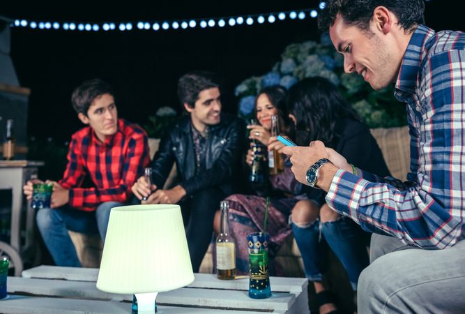 Happy man looking at smartphone at a party with friends