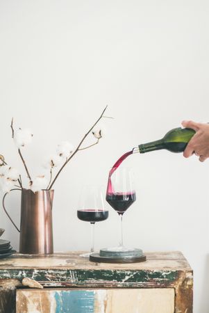 Wine glasses being poured from bottle with dried cotton in vase, vertical composition, copy space