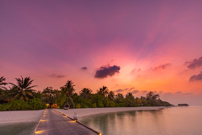 Landscape shot of lit up walkway to a beach at a sunset