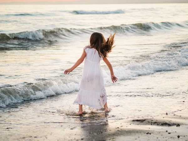 Adorable girl walking on seaside at sunset
