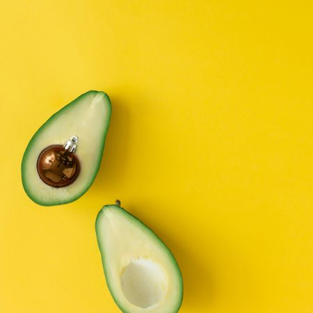 Avocado with brown bauble decoration in place of pit on bright yellow background