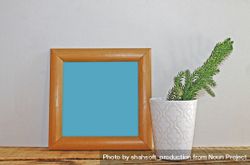 Plain square wooden picture frame with blue interior leaning against wall mockup 5l9L64