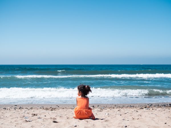Little girl sitting on beach and admiring view