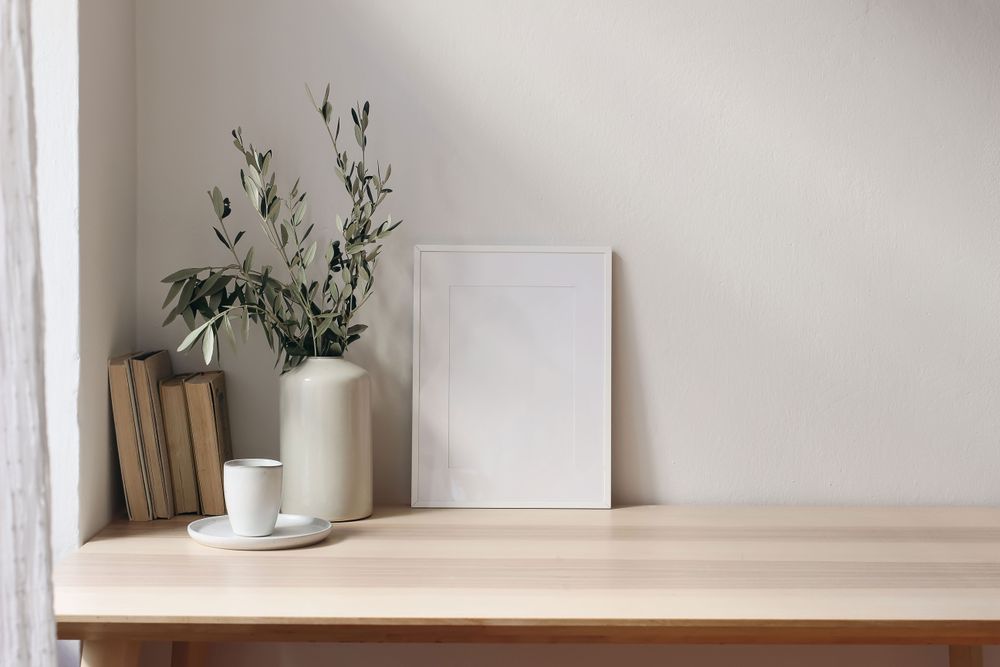 Elegant vase with olive tree branches on wooden table next to blank picture frame