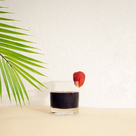 Cold drink with red strawberry under a palm leaf