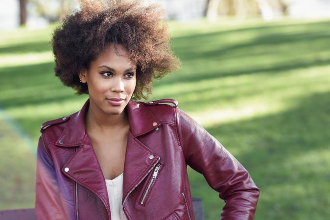 Woman sitting outside in red leather jacket on bright day with grass in background