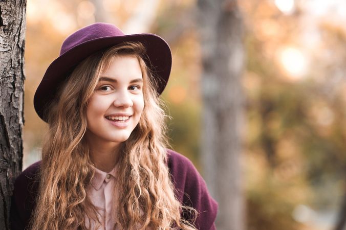 Portrait of smiling teenage girl with purple hat standing beside tree