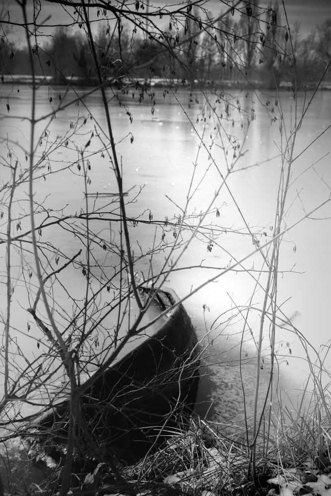 Monochrome shot of boat on frozen lake pictured through branches
