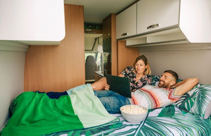 Male and female reclining on bed in motorhome with popcorn and digital tablet