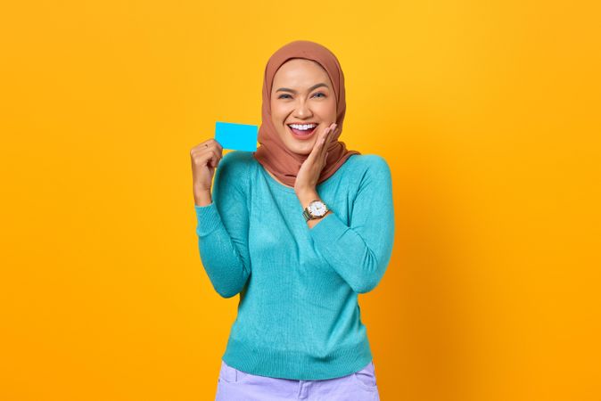 Muslim woman smiling while holding credit card with hand on side of her face