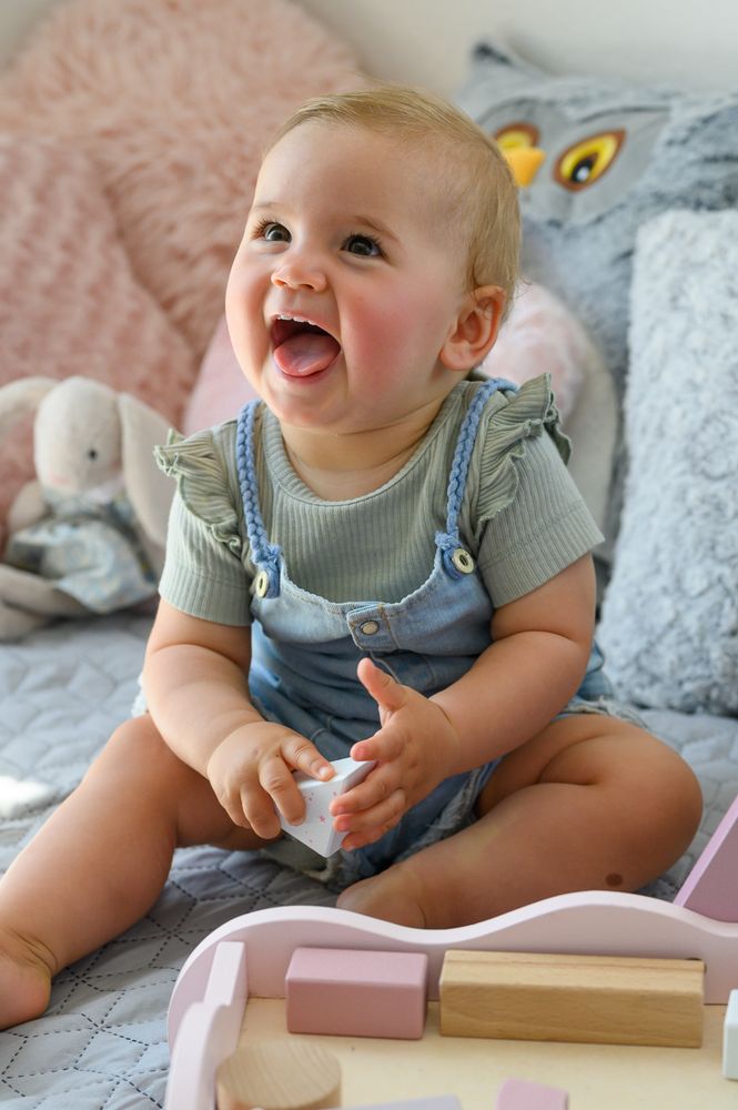 Cheerful baby playing with toy on bed