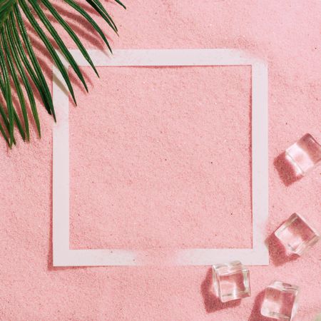 Pink sand with paper square outline and ice cubes and palm leaf