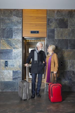 Mature man and woman outside of hotel elevator with luggage