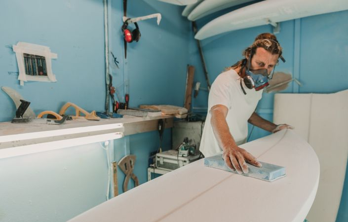 Man in respirator polishing surf board in workshop