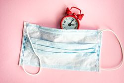 Clock and facemask on pink pastel background