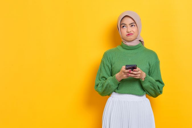 Frustrated woman in headscarf smiling and looking up from her smart phone