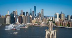 Iconic New York City Landscape Over East River with Skyscrapers, Brooklyn Bridge, Cars and Ferry Boats. Cinematic Urban Skyline with Clear Blue Sky