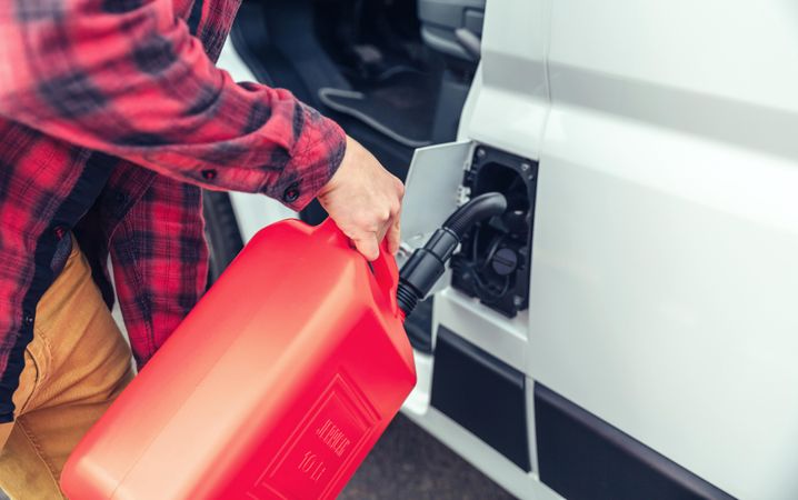 Male in red checkered shirt filling up van with gas can, closeup